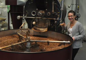 Manufakturen-Blog: Cornelia Dotschat neben dem Trommelröster - davor wird der frisch geröstete Kaffee mit kalter Luft auf einem großen Rost abgekühlt, damit der Röstvorgang stoppt (Foto: Wigmar Bressel)